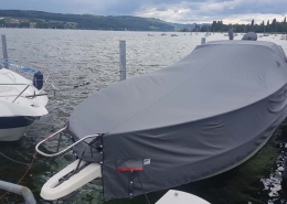 Persenning 1 Motorboot mit grauer Ganzpersenning am Steg vor Seepanorama